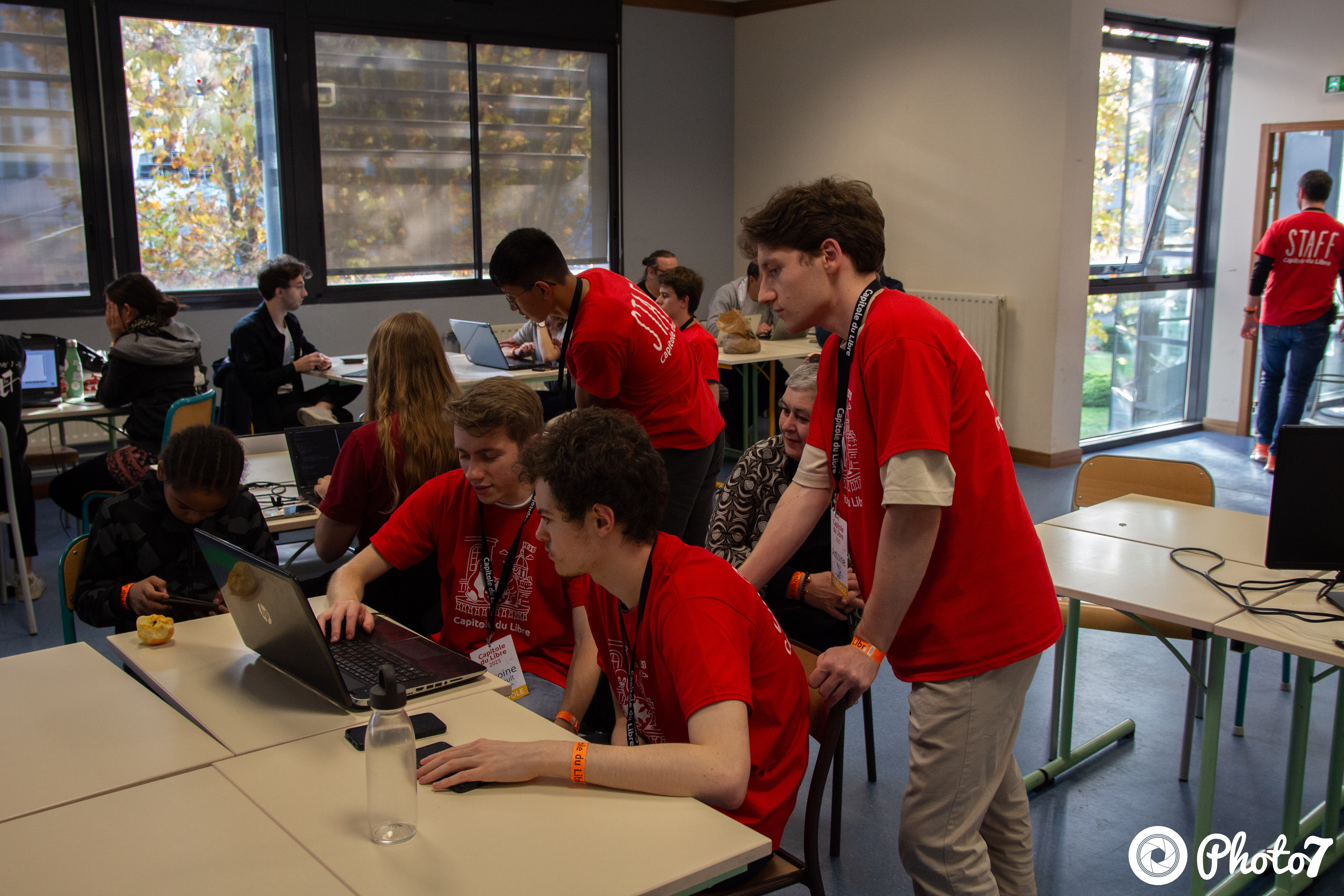 Jeunes bénévoles en t-shirt rouge aidant un participant sur son laptop