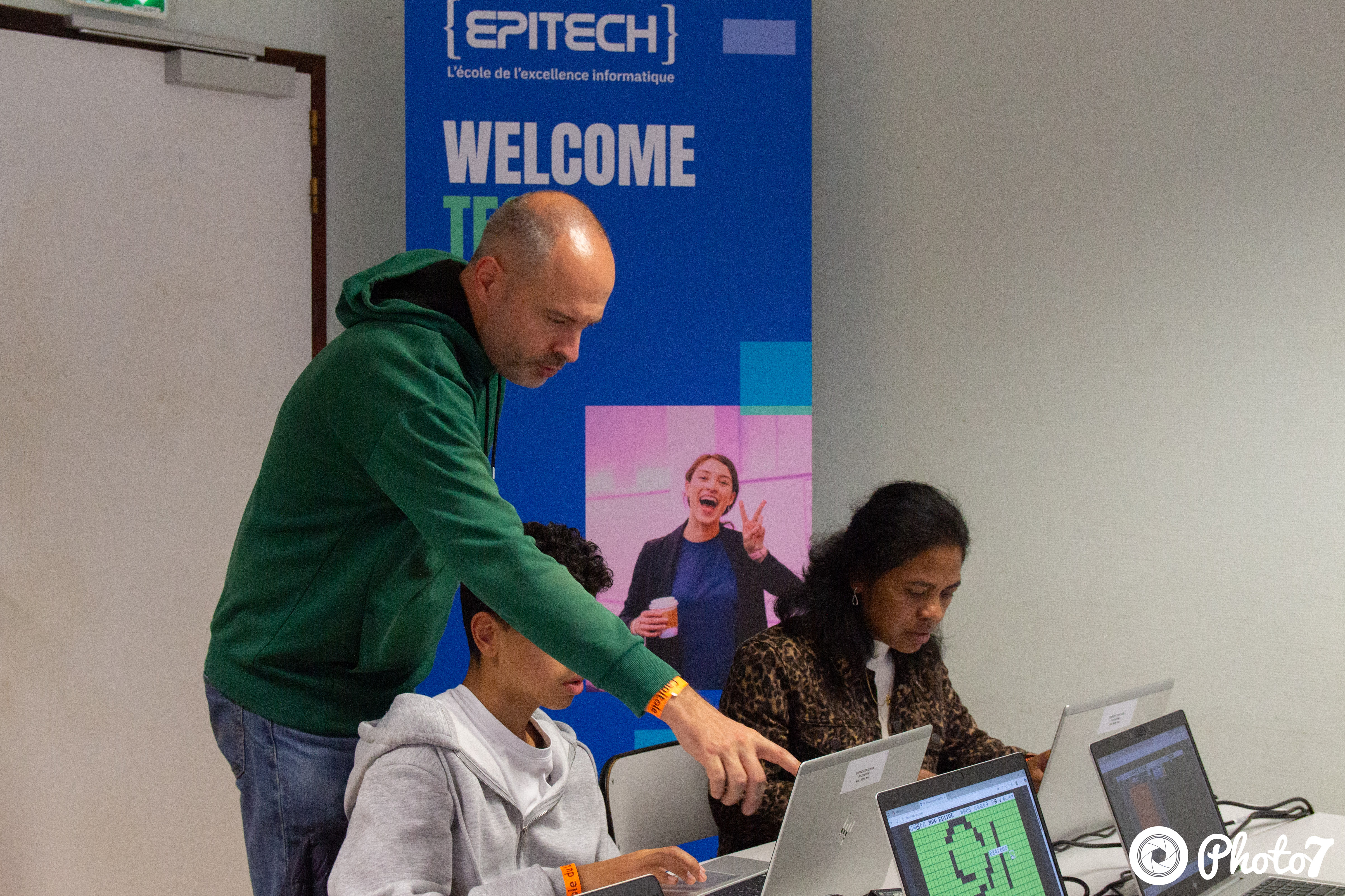 Bénévole aidant un enfant et une participante sur des ordinateurs portables