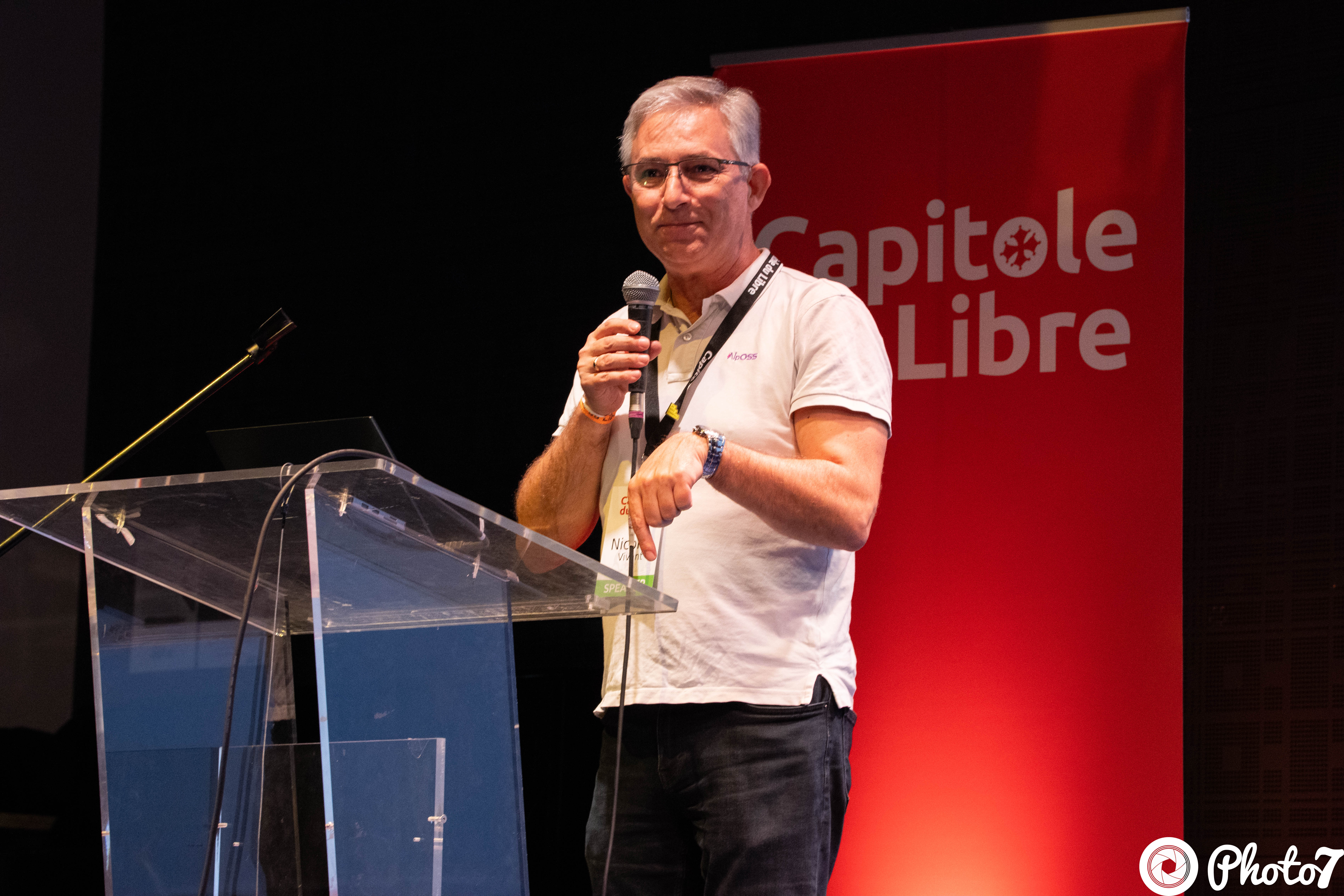 Speaker au pupitre transparent avec micro, banner Capitole du Libre