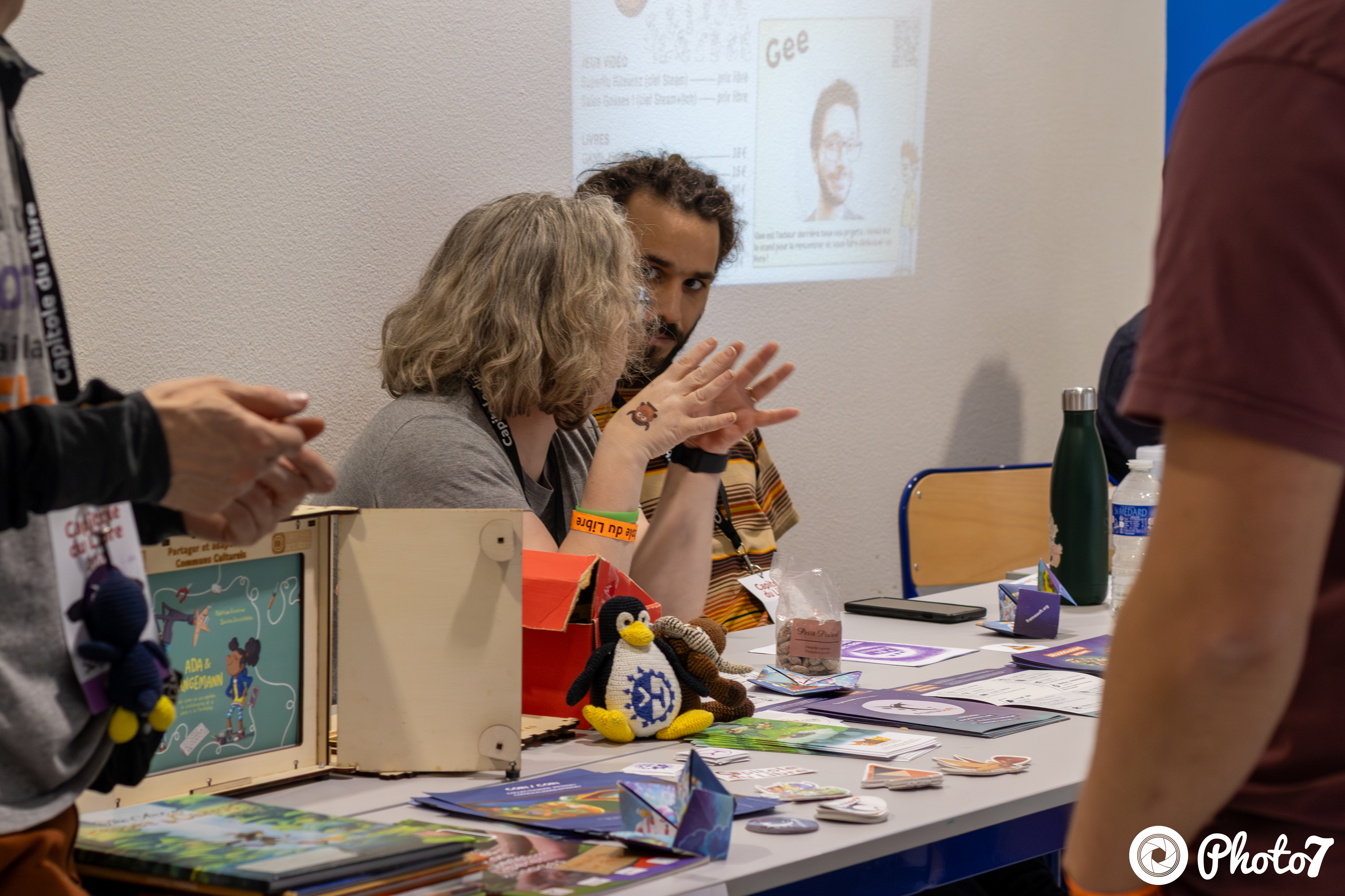 Stand avec peluche Tux et badges, exposant en pleine discussion