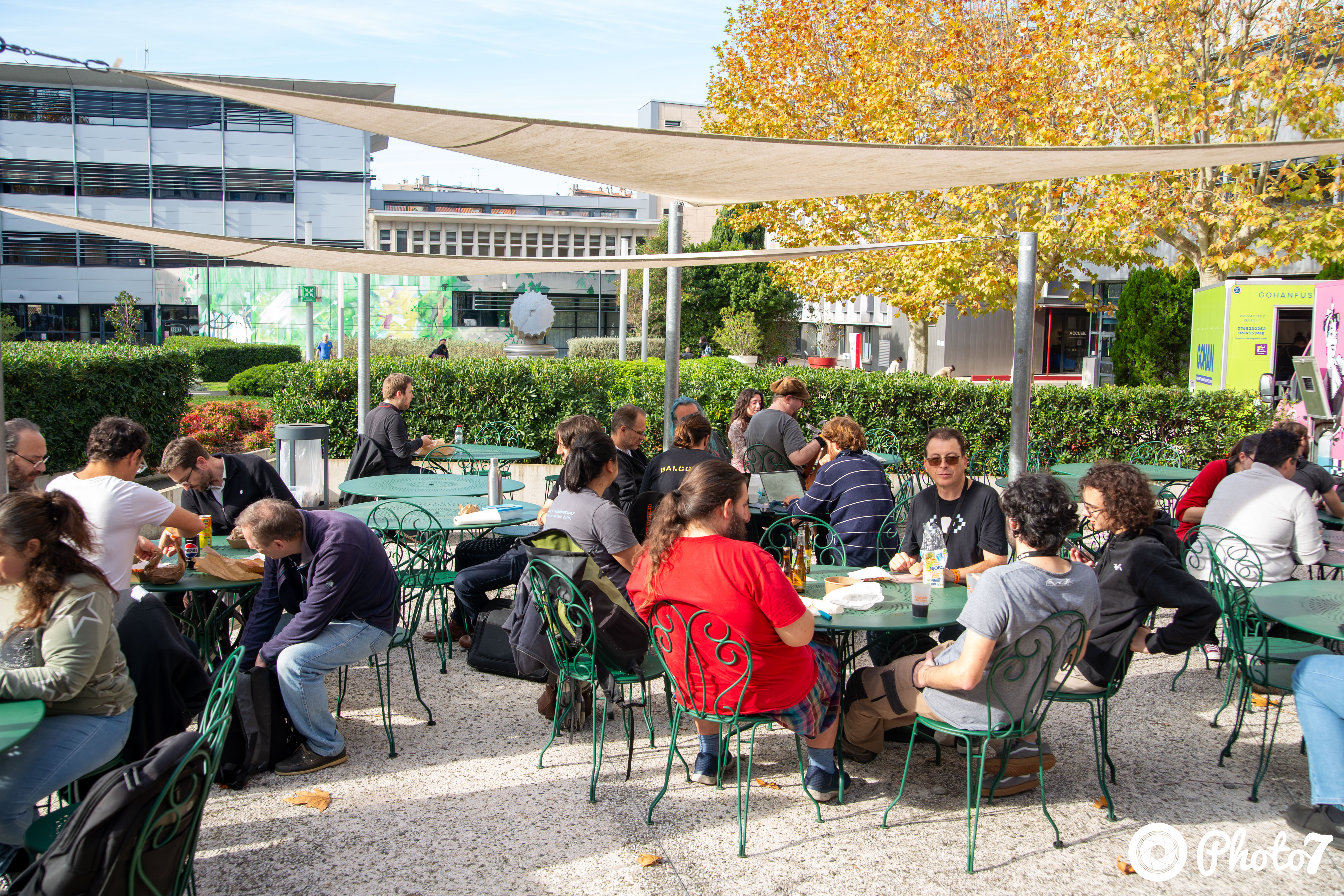 Participants déjeunant en extérieur sous les voiles d'ombrage avec food trucks en arrière-plan